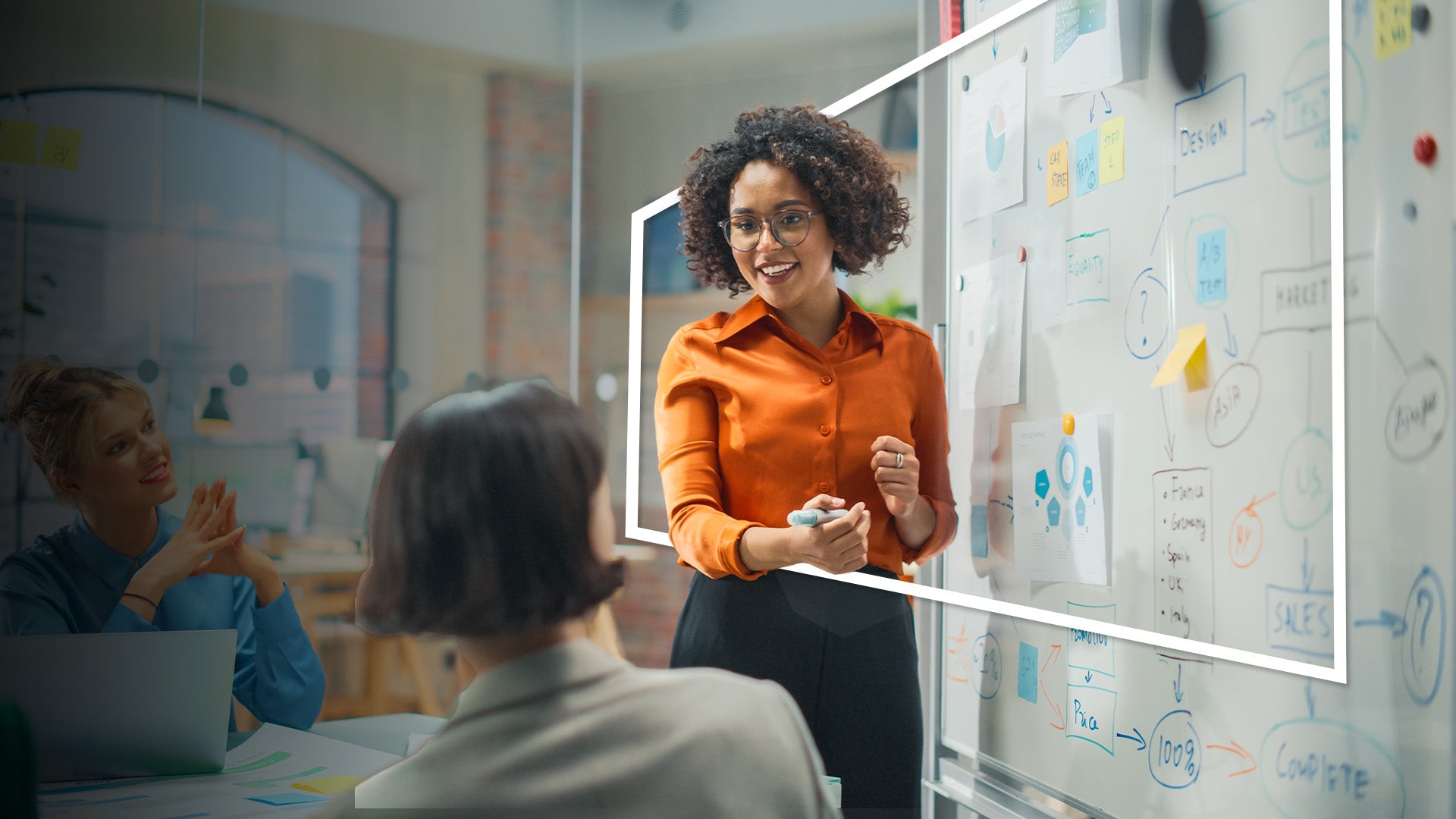 A professional woman in an orange blouse presents risk assessment strategies on a whiteboard to colleagues in a modern office, reflecting expertise in global work and travel personal accident insurance solutions.