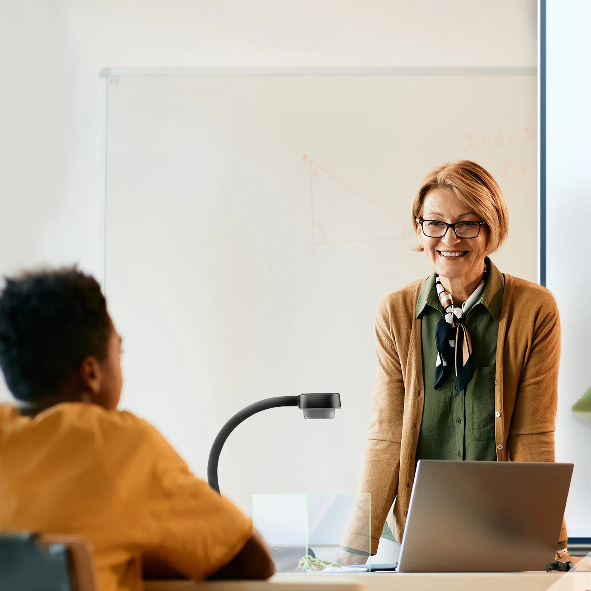Discover the AVerVision F17+ visualiser in action as a teacher engages a student at a desk with laptop and classroom whiteboard.