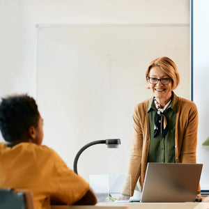 Discover the AVerVision F17+ visualiser in action as a teacher engages a student at a desk with laptop and classroom whiteboard.