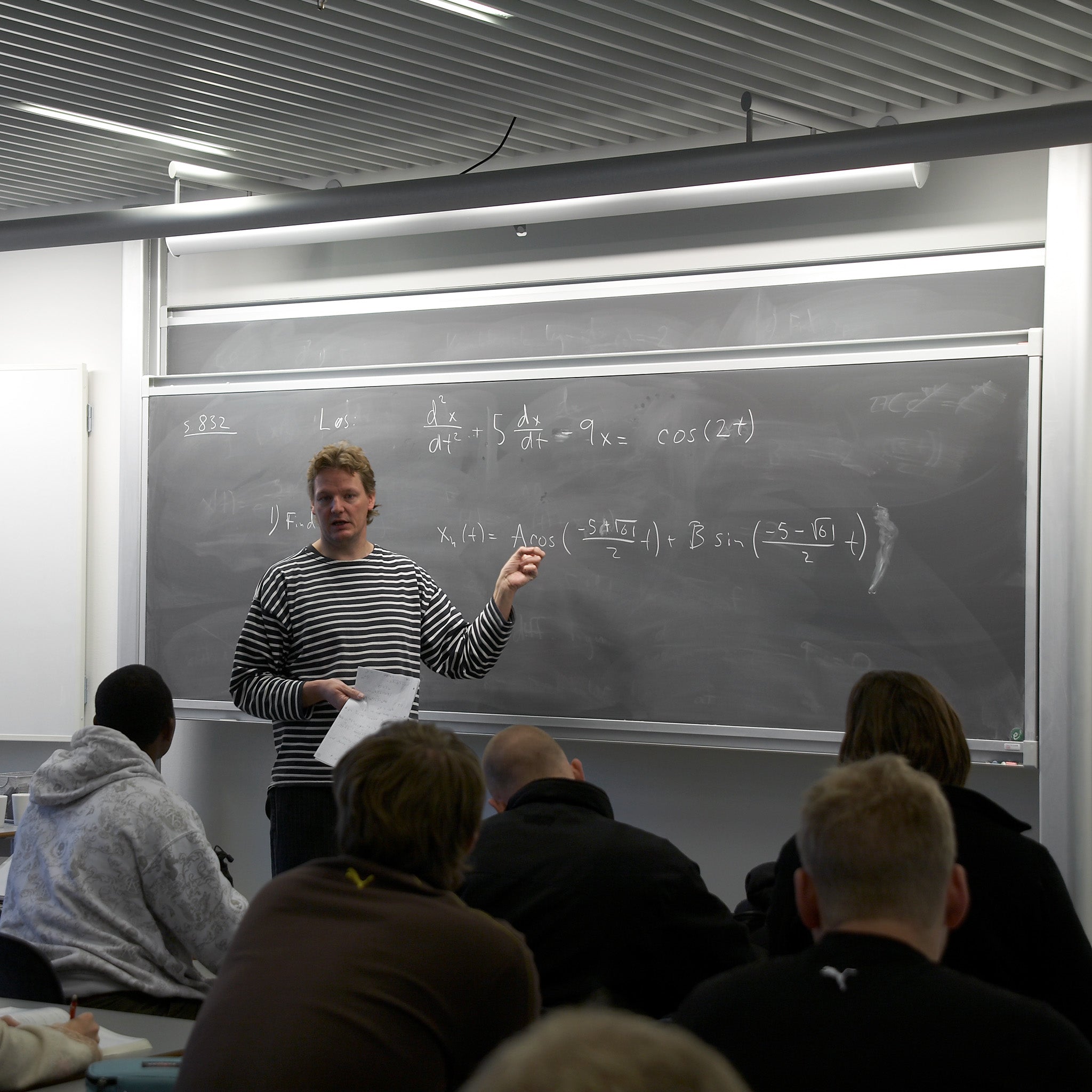 A teacher in a striped sweater teaches math to students using the innovative Presentation Spaces Electric Chalk Column Board.