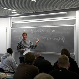 A teacher in a striped sweater teaches math to students using the innovative Presentation Spaces Electric Chalk Column Board.