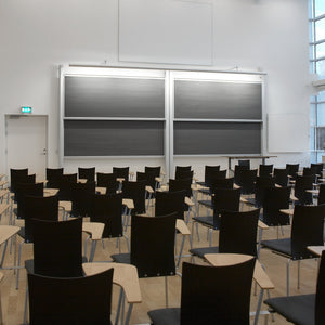 Modern lecture hall with black chairs, desks, and Electric Chalk Column Boards by Presentation Spaces; bright white walls, large windows.