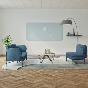 Modern office lounge with blue chairs, coffee table, Chameleon Curve frameless whiteboard, wood herringbone floor, and plant.