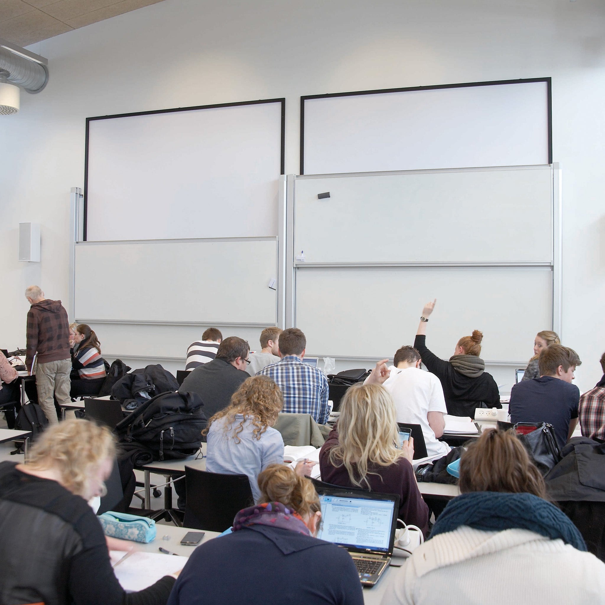 Students in a bright, modern classroom use laptops and notebooks, engaging with Presentation Spaces Dry Wipe Column Boards.
