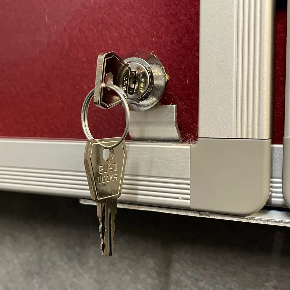 EURO LOCKS key in a fire-rated Eco FR Tamperproof Felt Noticeboard, red and silver, aluminium frame, secure keychain visible.