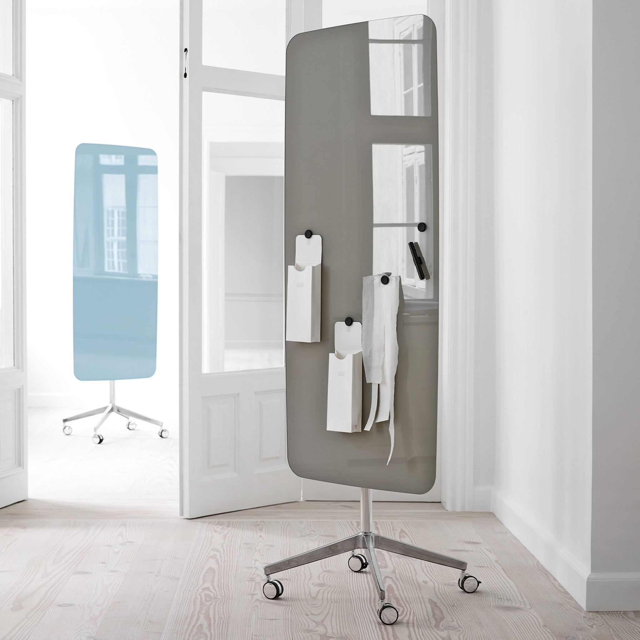 Modern office with Lintex Flow Mobile glassboards in gray and blue, magnetic surfaces displaying notes, on light wood floors, white walls.