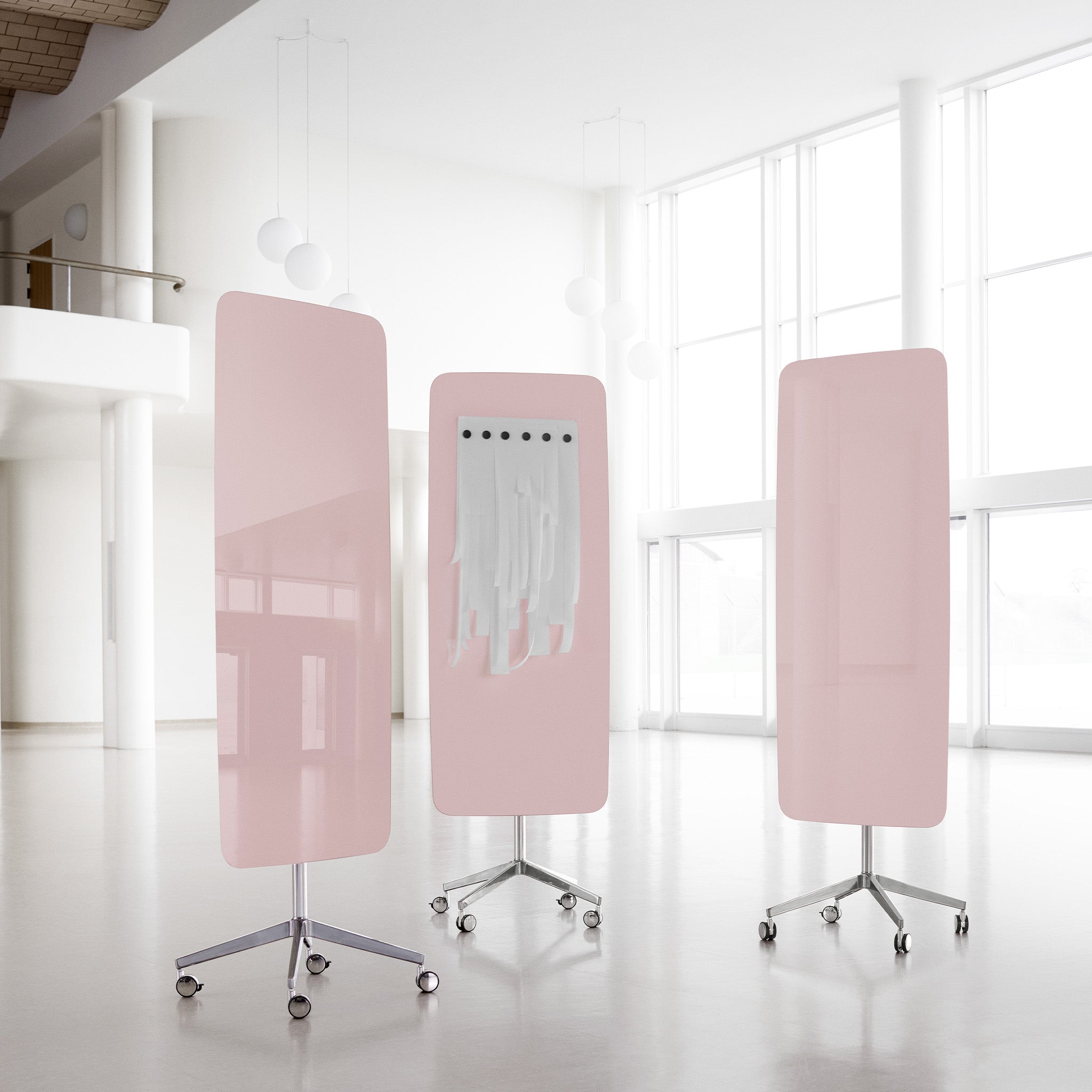 Showcasing three pink Lintex Flow Mobile glassboards with rounded edges in a bright, modern office; one features white fabric strips.