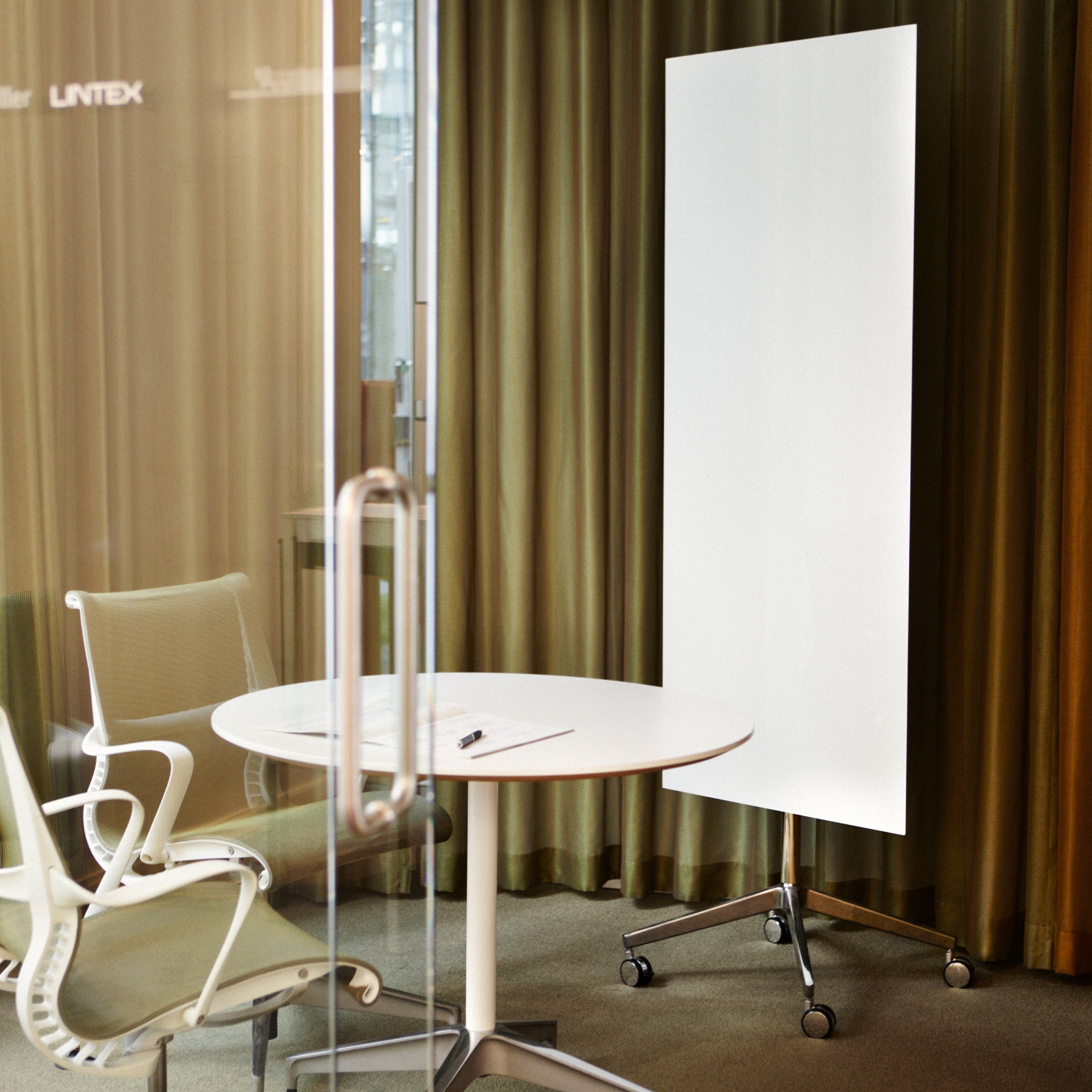 Discover a sleek office with Lintex Mood Mobile glassboard, round white table, chair, and glass door—perfect for modern workspaces.