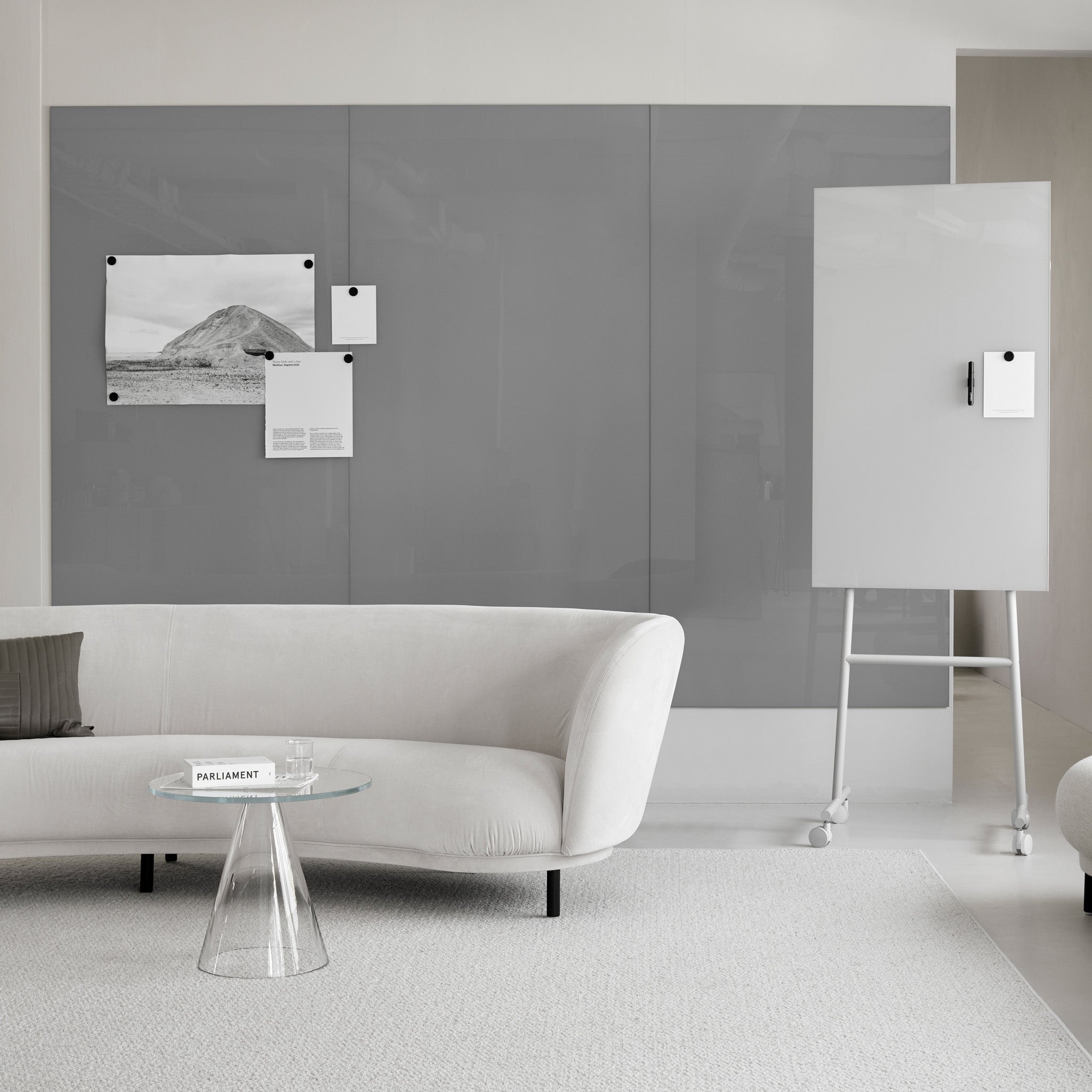 Modern minimalist office with Lintex Mood Spaces magnetic glass board, white sofa, glass table, and mobile whiteboard on carpet.