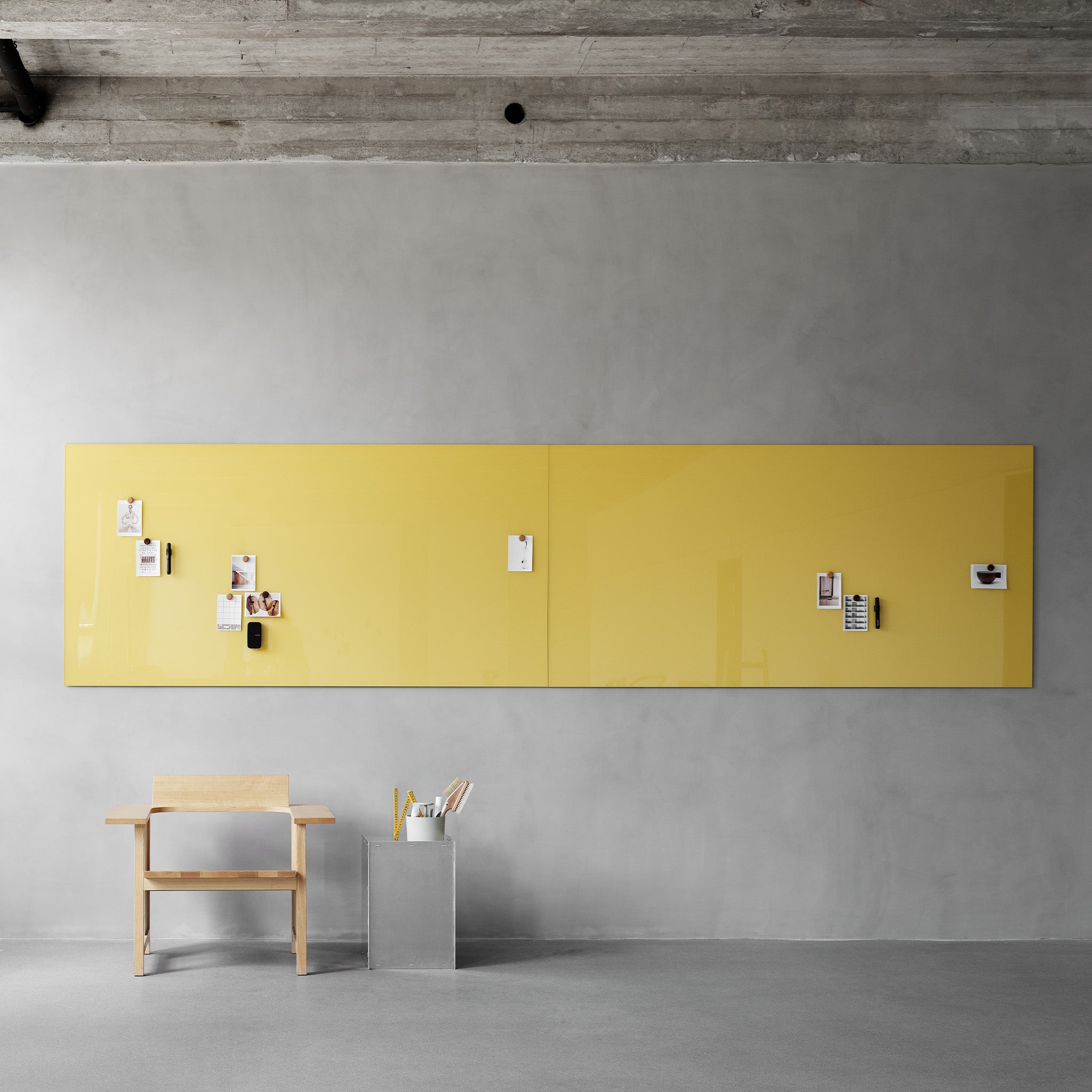 Minimalist office with concrete ceiling, gray walls, yellow Lintex Mood Spaces magnetic glass board, wooden desk, and pen holder.