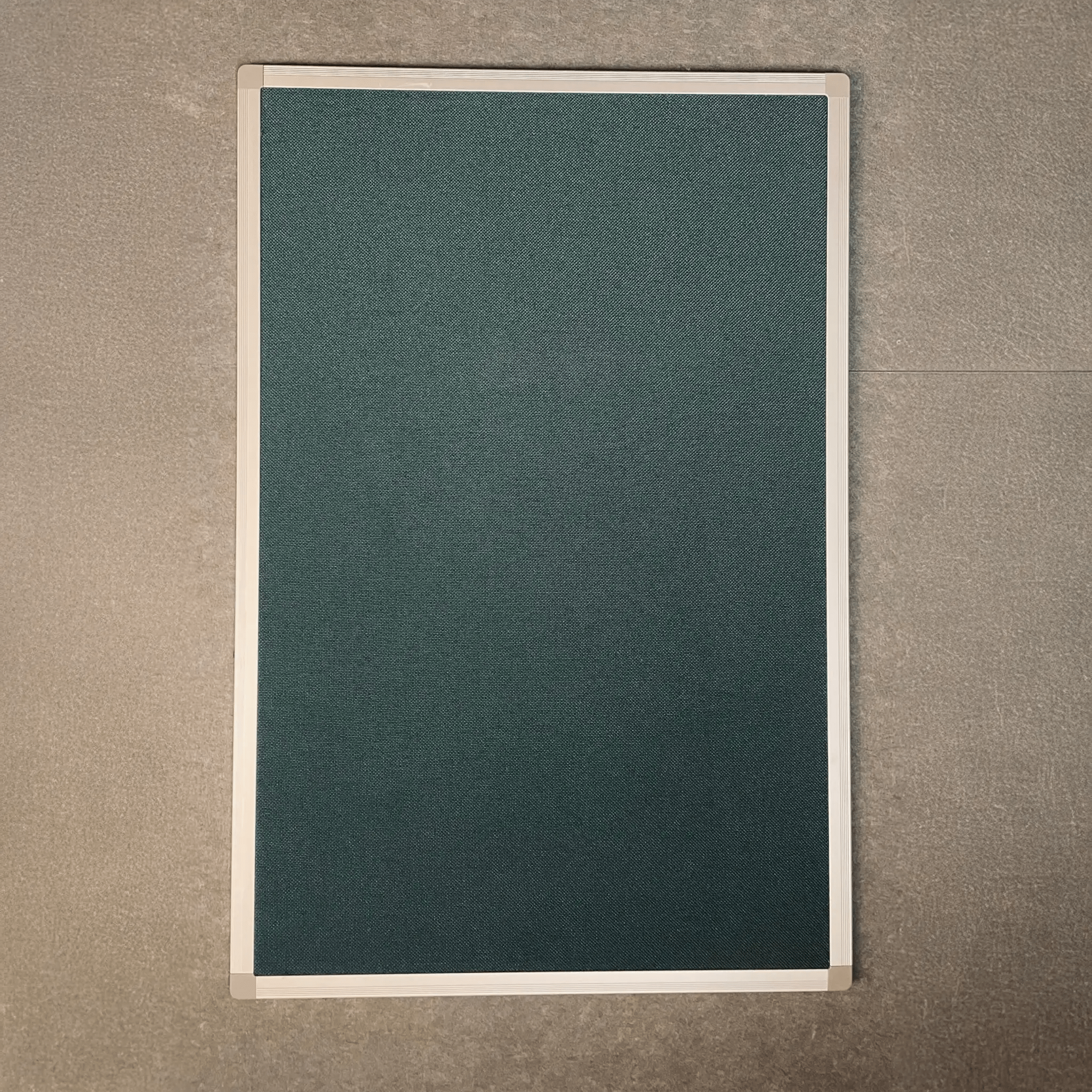 Class 1 fire rated Premier Camira Cara Notice Board with green fabric, aluminium frame, on gray textured wall by Presentation Spaces.