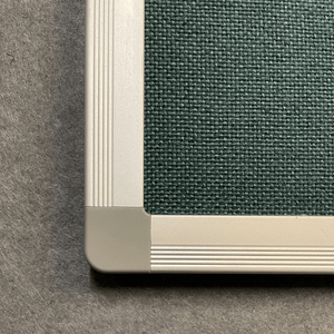 Close-up of Premier Camira Cara Notice Board’s green Class 1 fire-rated fabric and aluminium frame on a grey textured backdrop.