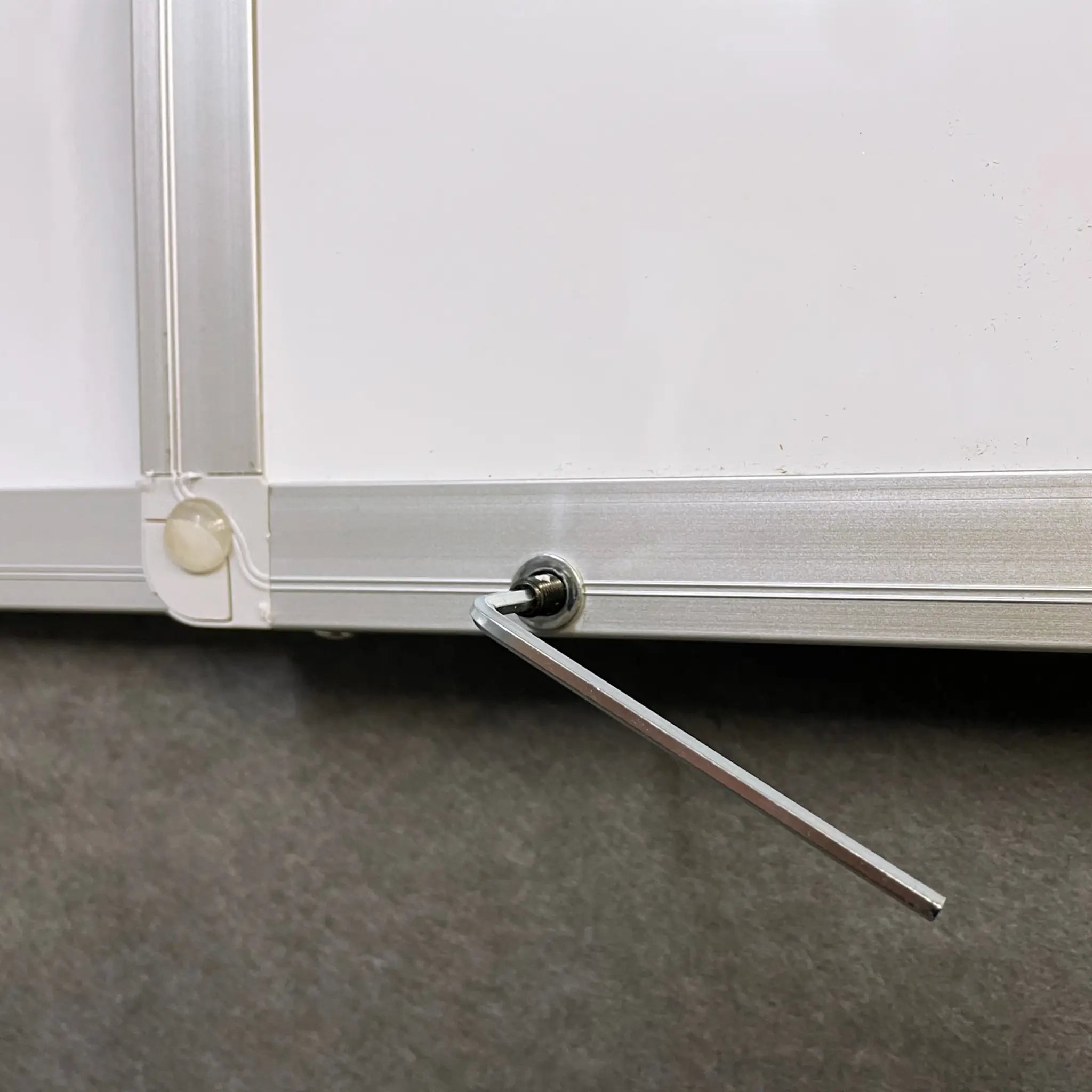 Close-up of Presentation Spaces FR Confidential Lockable Non-Magnetic Whiteboard corner, silver frame, hex key adjusting screw.