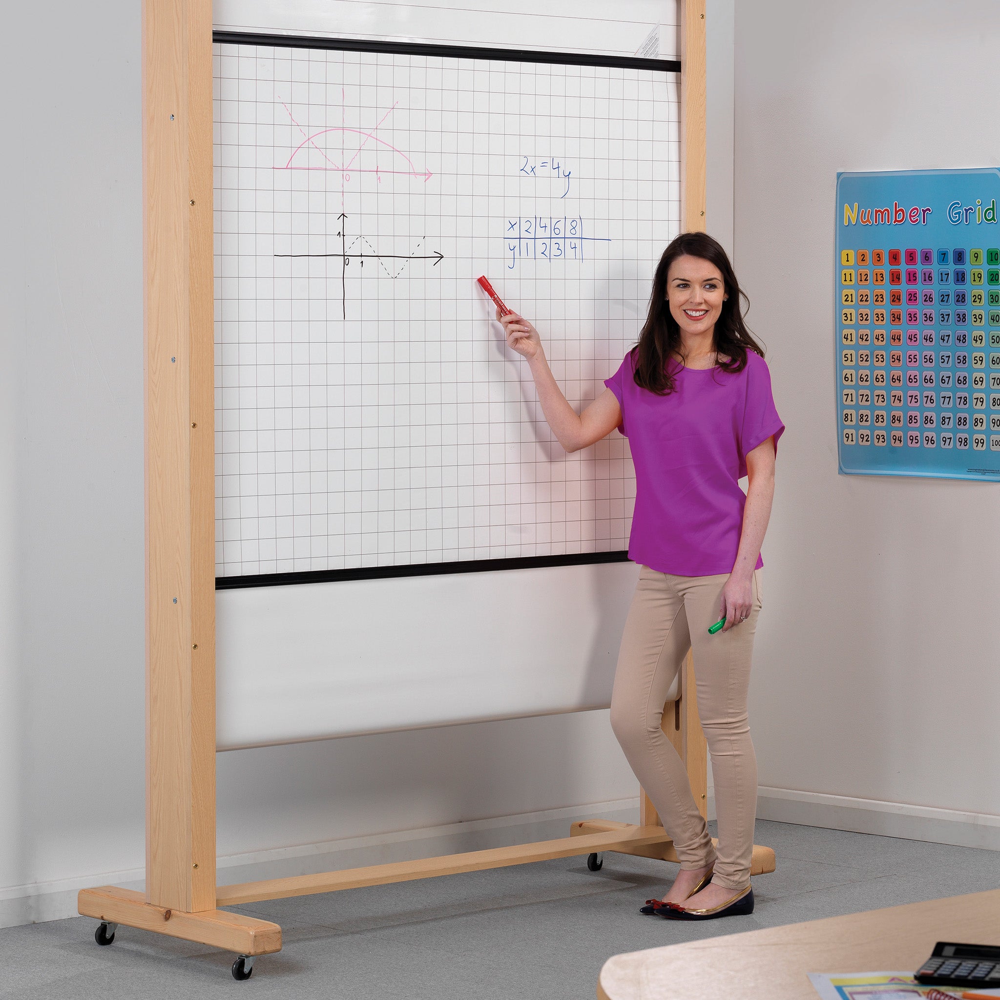 Teacher in purple top demonstrates math on Presentation Spaces Mobile Rollerboard Frame; number grid, teaching aids also shown.