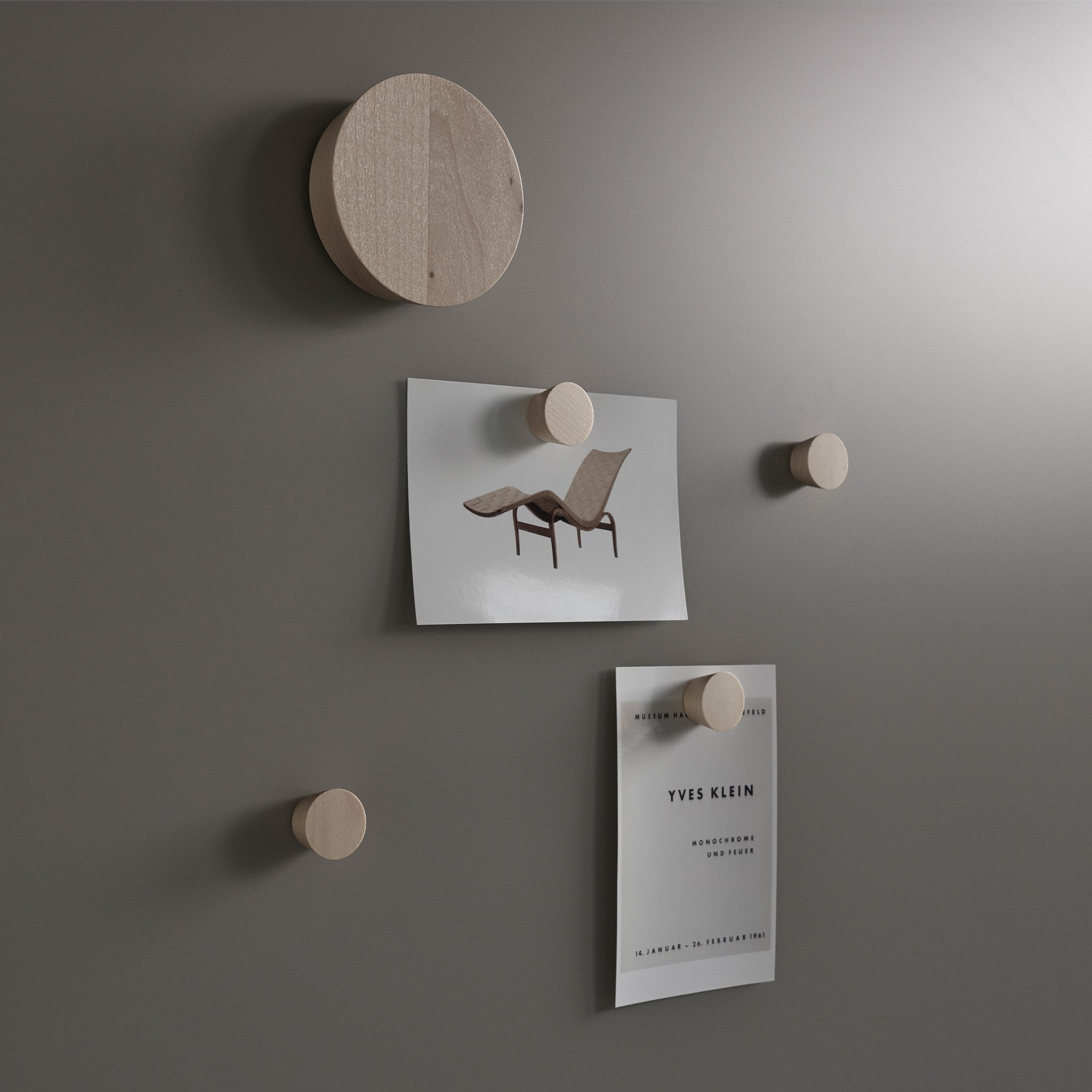 Modern matte gray Lintex Silk Wall with five wooden pegs displays a lounge chair photo and Yves Klein minimalist exhibition flyer.