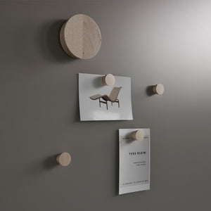 Modern matte gray Lintex Silk Wall with five wooden pegs displays a lounge chair photo and Yves Klein minimalist exhibition flyer.