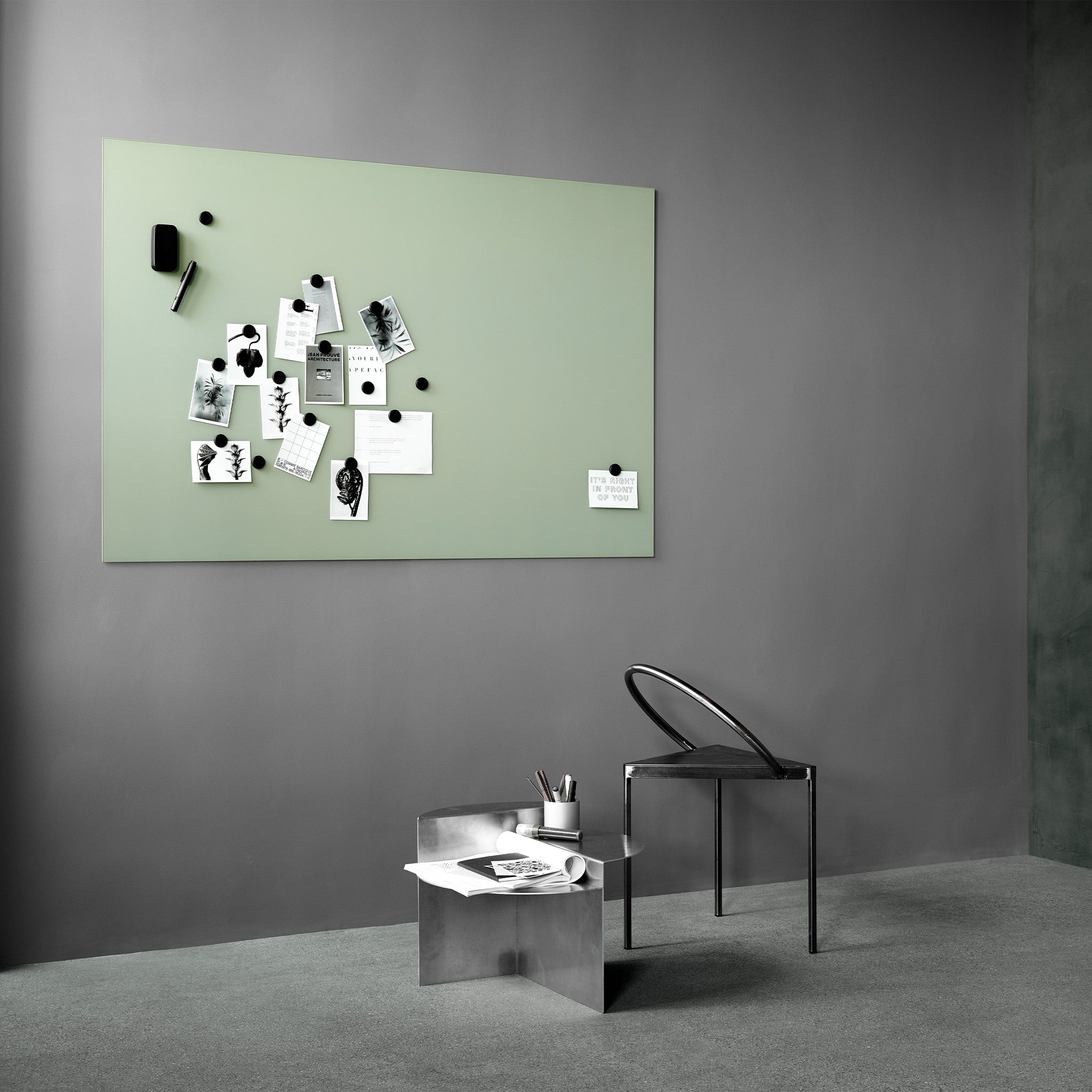Modern minimalist office with black chair, metallic desk, stationery, and Lintex Silk Wall—green matte glassboard used as bulletin board.