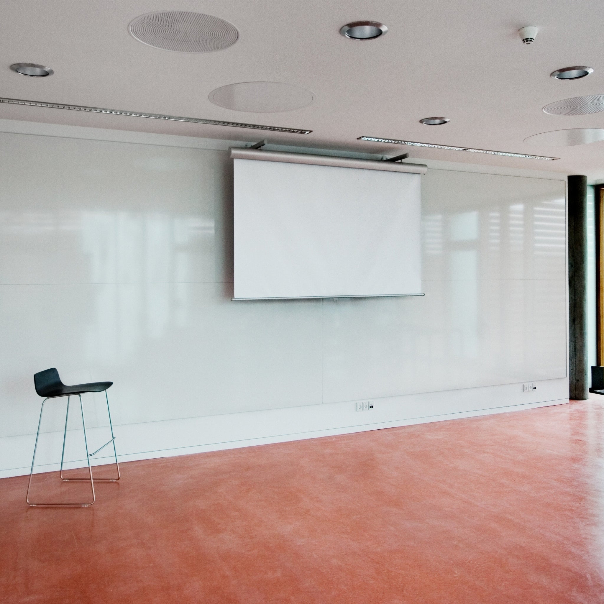 Discover our modern room with a red floor, premium unframed writing wall, projector screen, and sleek black barstool.