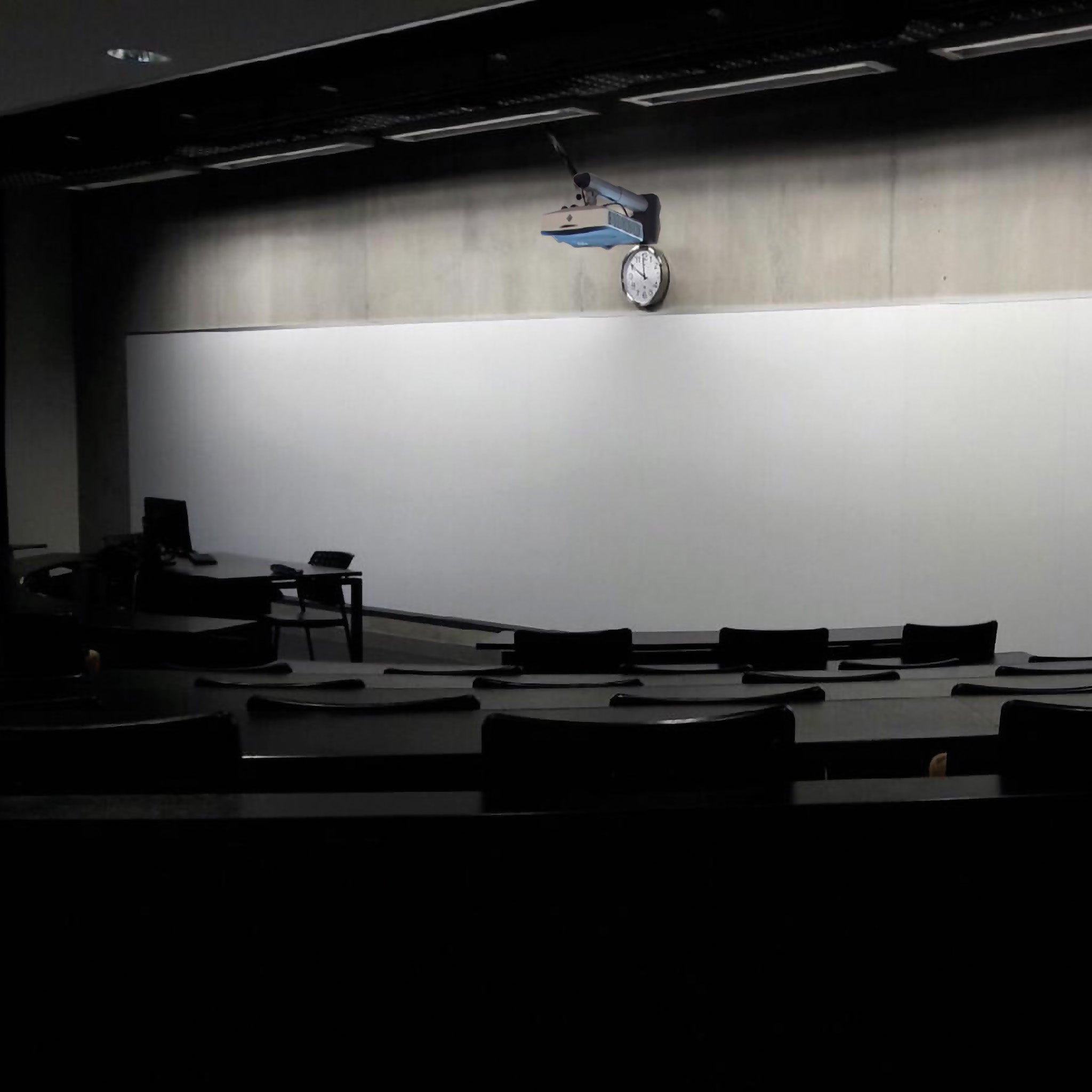 A modern classroom with a Presentation Spaces Dry Wipe Writing Wall, clock, projector, and rows of black desks and chairs.