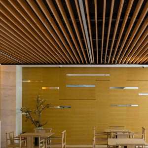Modern dining area with wood tables, yellow cutout walls, stylish décor, and Zen Beam acoustic baffles for optimal sound control.