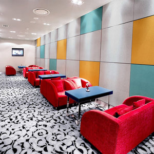 Modern lounge with red sofas, blue tables, and Zen Zone’s Zen Liner acoustic panels, plus patterned carpet and wall-mounted TV.