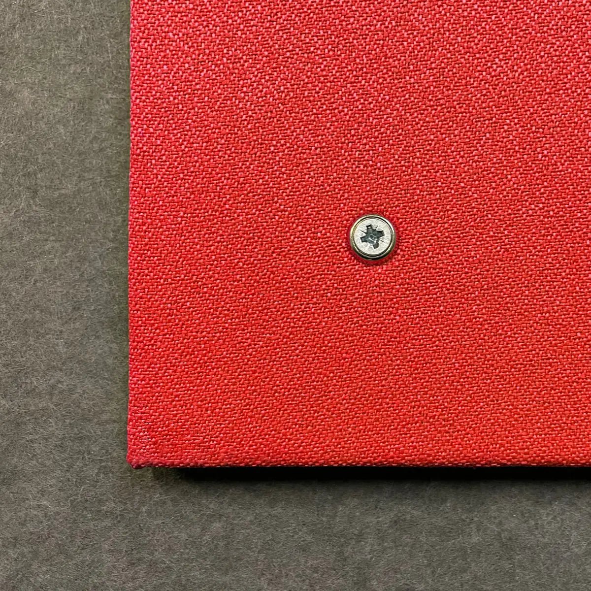 Close-up of red Premier Camira Lucia Unframed Notice Board by Presentation Spaces; Class 1 Fire Rated, silver screw, dark gray background.