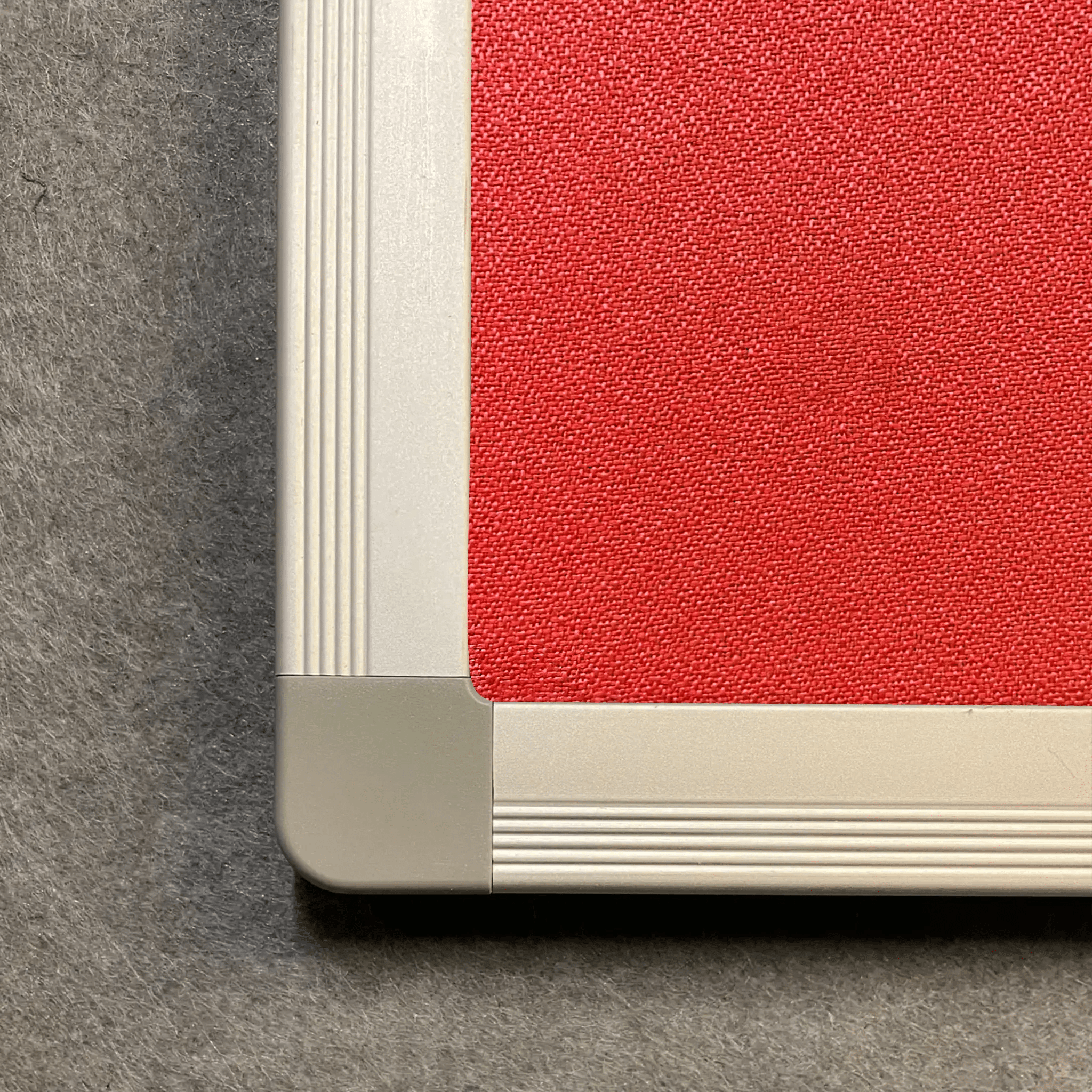 High-quality close-up of a Premier Camira Lucia aluminium-framed notice board, red surface, Class 1 Fire Rated, beige frame.
